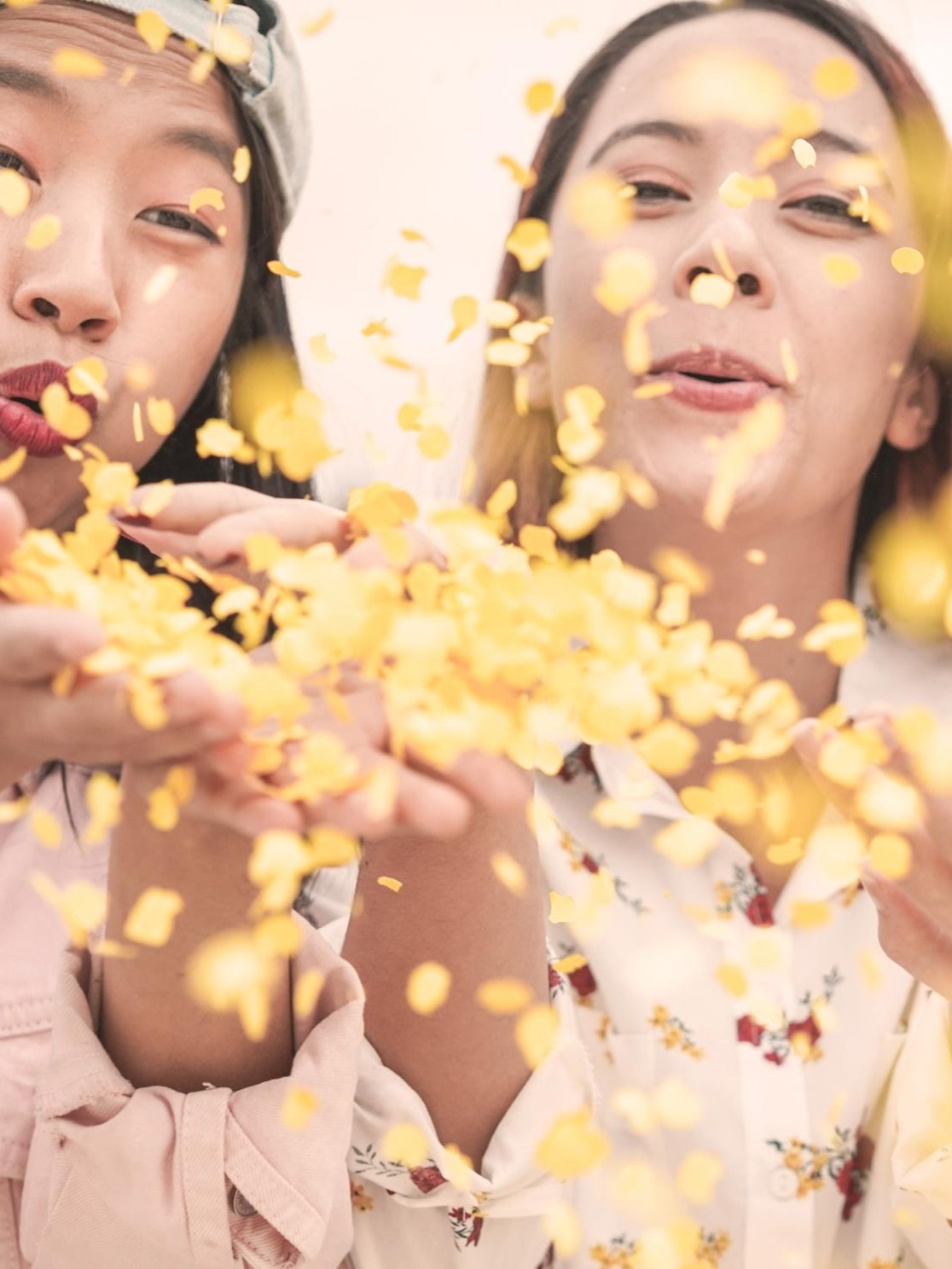 Drei junge Frauen blasen lachend goldene Konfetti in die Kamera