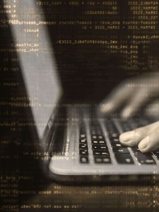 Die Hände einer Person tippen auf einem Laptop. Das Bild ist braun-gräulich gefärbt.