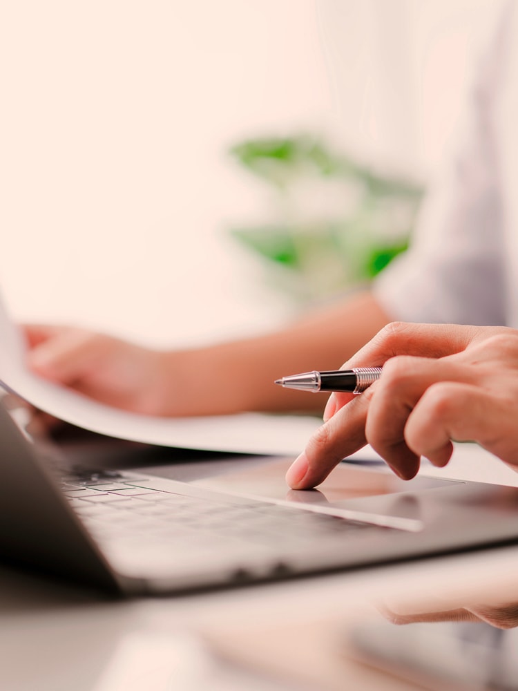 Ein Unbekannter arbeitet am Laptop und hält in einer Hand ein Papier und in der anderen einen Stift