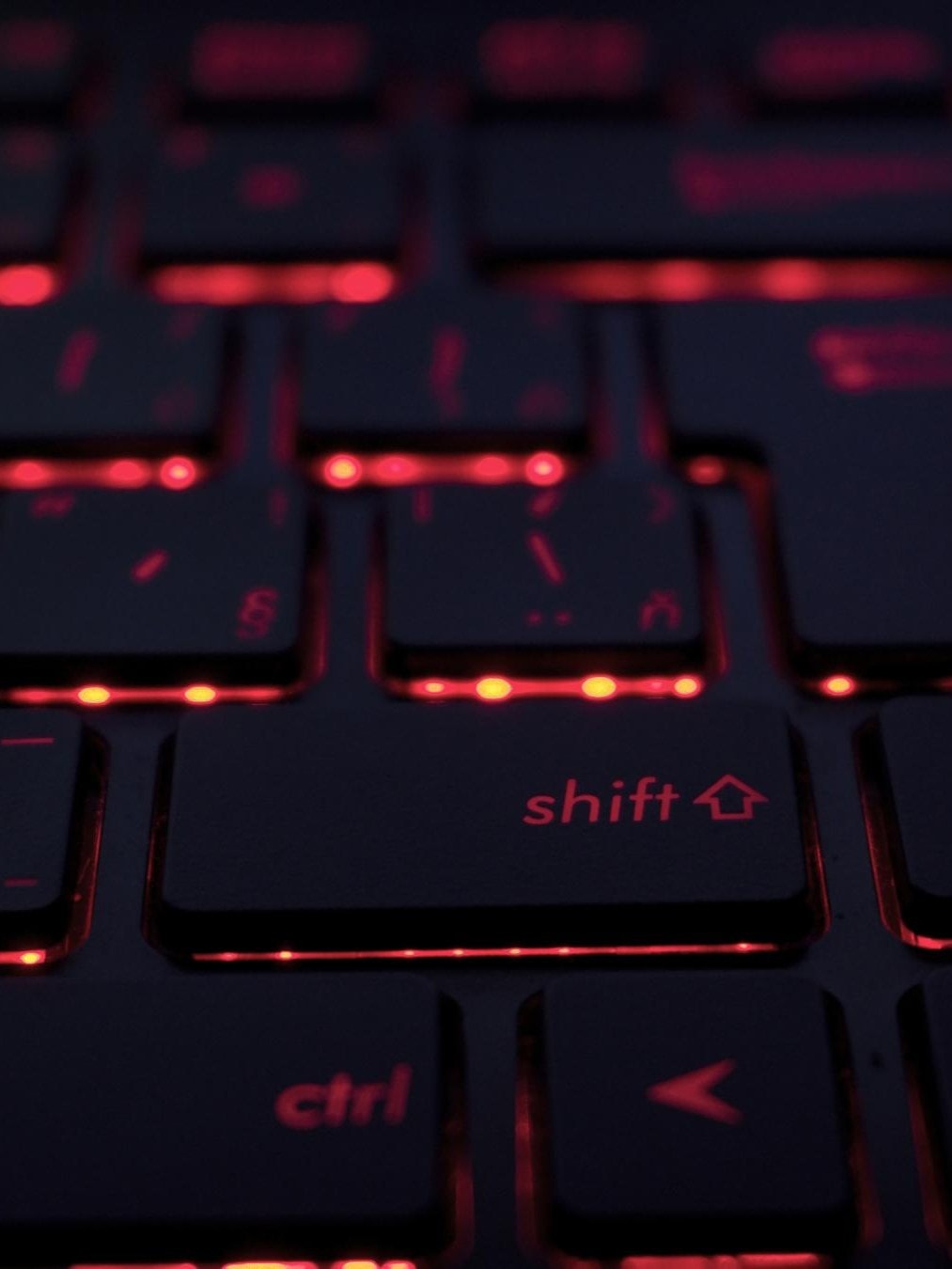 Eine Nahaufnahme einer Tastatur mit roter Hintergrundbeleuchtung. Die Tasten sind schwarz und die rote Beleuchtung scheint durch die Buchstaben und Symbole auf den Tasten hindurch.
