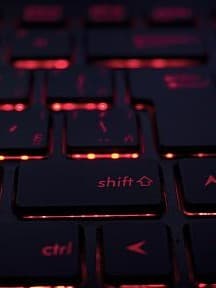 Eine Nahaufnahme einer Tastatur mit roter Hintergrundbeleuchtung. Die Tasten sind schwarz und die rote Beleuchtung scheint durch die Buchstaben und Symbole auf den Tasten hindurch.