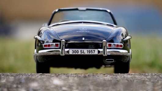 Rückansicht eines klassischen schwarzen Mercedes-Benz 300 SL Cabriolets aus dem Jahr 1957 auf einer Straße, mit einem Nummernschild mit der Aufschrift „300 SL 1957“ vor einem unscharfen Hintergrund im Freien.