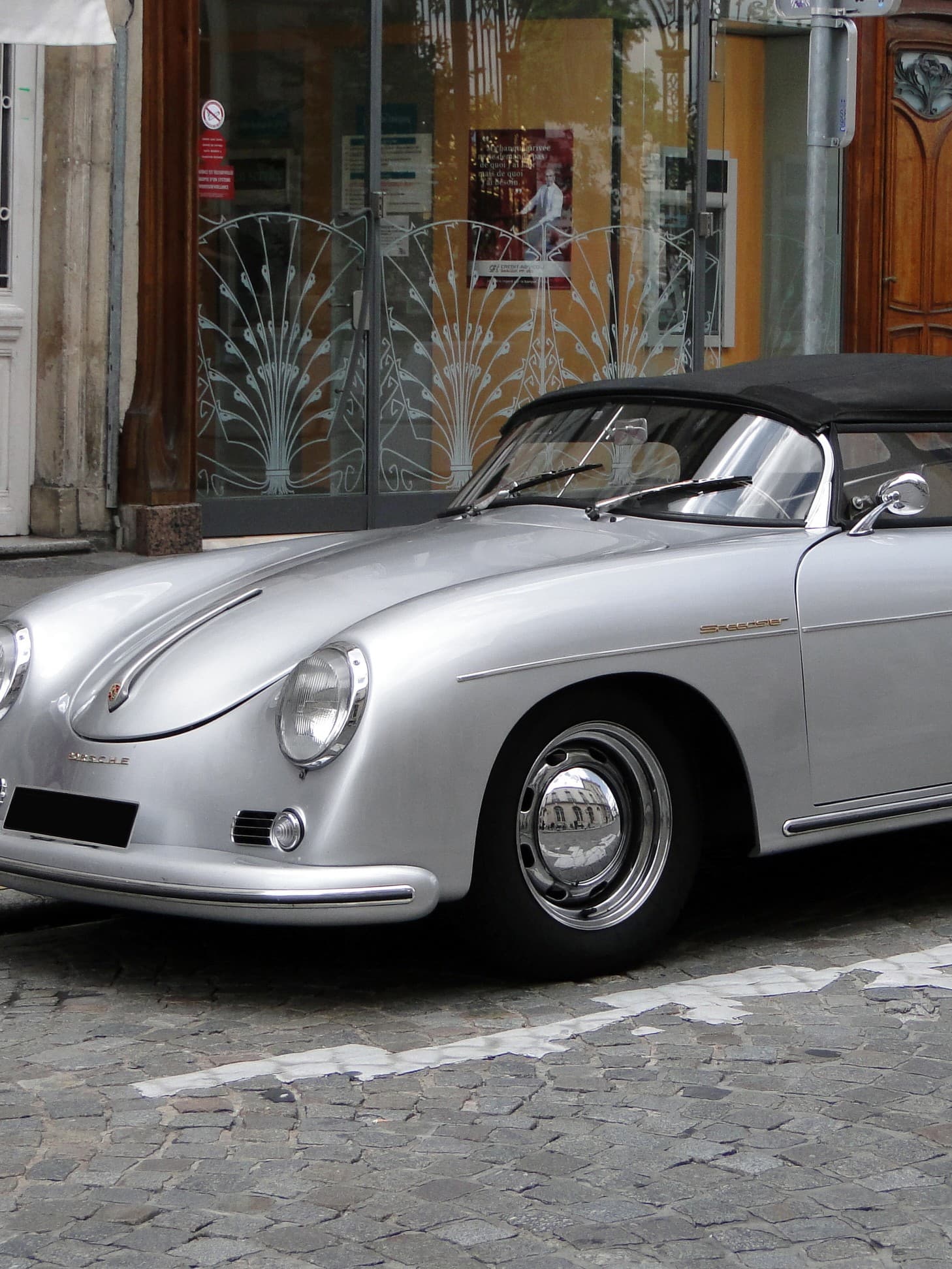 Ein leuchtend gelbes Oldtimer-Cabrio Alfa Romeo Spider mit zwei Insassen fährt während einer Veranstaltung eine Straße entlang. Die Szene ist lebhaft, im Hintergrund stehen Schaulustige.