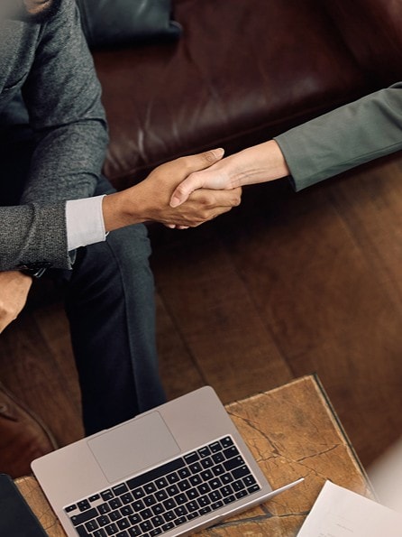 Geschäftsführer sitzt auf einem Ledersofa vor einem Laptop und schüttelt einer Mitarbeiterin die Hand