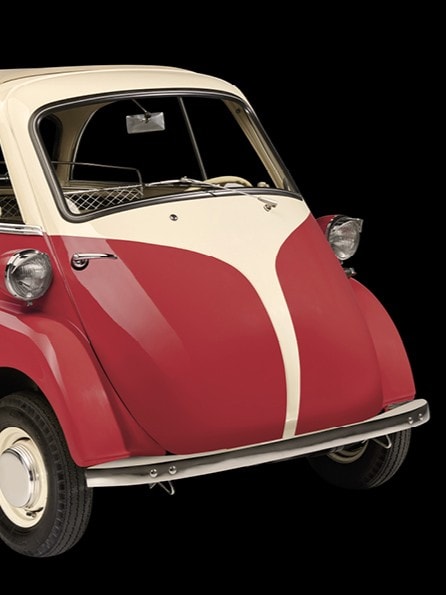 Ein klassisches Mikroauto, ein BMW Isetta, mit roter Karosserie und weißen Akzenten. Es hat eine nach vorne öffnende Tür und kleine runde Scheinwerfer.