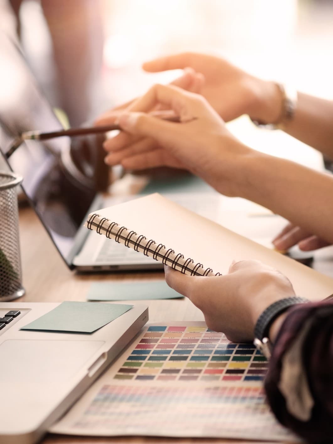 Zwei Personen arbeiten an einem Schreibtisch. Eine Person zeigt auf einen Laptop-Bildschirm.