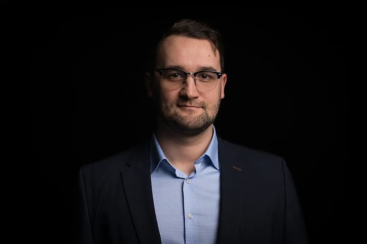 Klemens Lemke ist im Anzug und mit Brille vor einem dunklen Hintergrund. Er trägt einen marineblauen Blazer und ein hellblaues Hemd.