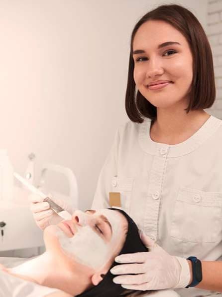 Eine Person in einem weißen Kittel und Handschuhen führt eine Fußbehandlung durch. Im Hintergrund sind verschiedene medizinische oder Spa-Geräte zu sehen.