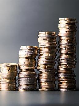 Gestapelte Münzen in verschiedenen Höhen, die von links nach rechts ansteigen. Die Münztürme symbolisieren ein wachsendes Vermögen. Hintergrund ist schlicht und grau gehalten.