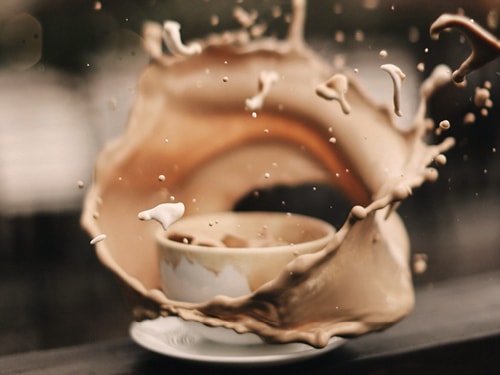 Eine Kaffeetasse die angestoßen wurde. Der Kaffee verspritzt heftig rund um die Tasse