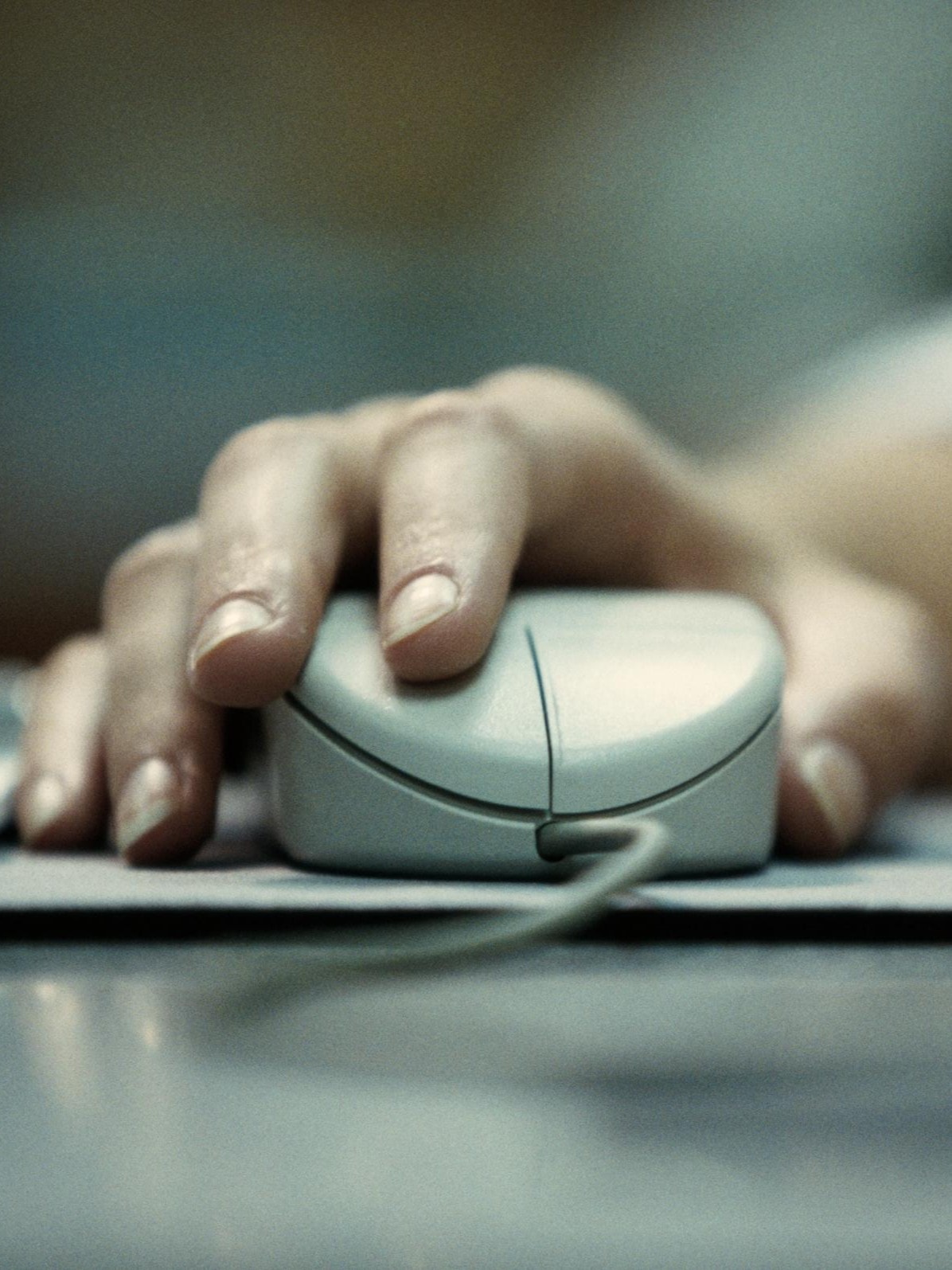 Eine Nahaufnahme einer Hand, die auf einer Computermaus ruht. Die Hand ist in Position, um die linke Maustaste zu klicken, und ein Kabel ist an der Vorderseite der Maus sichtbar.