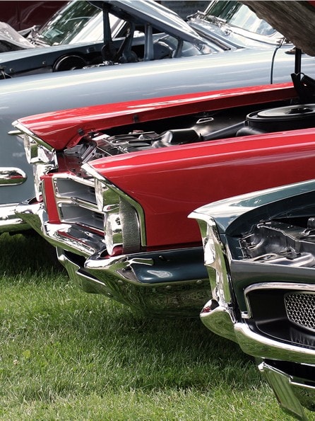 Vier Oldtimer mit offenen Motorhauben parken nebeneinander auf einer grünen Wiese