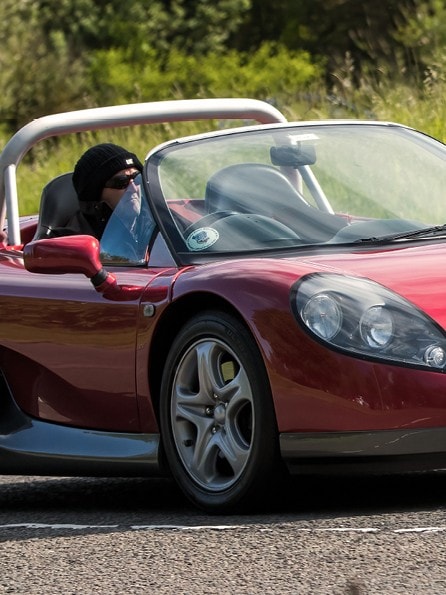 Zu den neue Oldtimer 2025 gehört der Renault Sport Spider. Hier in rot auf einer Straße mit Fahrer am Steuer.