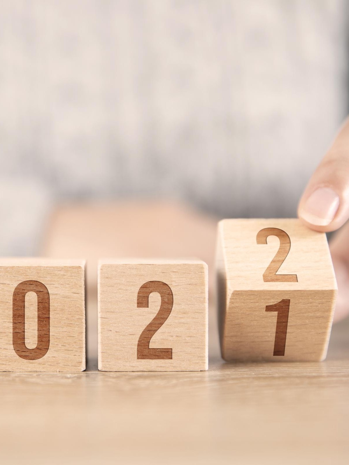 Vier Holzblöcke zeigen die Zahlen "2021". Eine Hand dreht den letzten Block, um die Zahl "1" in "2" zu ändern, was den Übergang von 2021 zu 2022 symbolisiert.