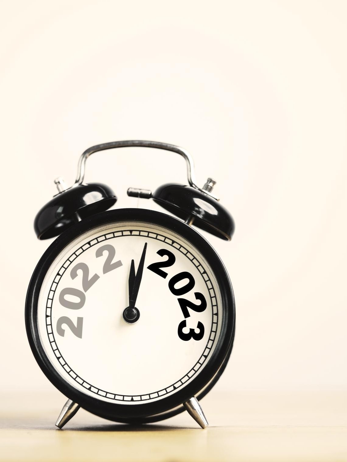 Ein schwarzer analoger Wecker mit den Jahren "2022" und "2023" auf dem Zifferblatt. Der Stundenzeiger zeigt auf 12 und symbolisiert den Übergang von 2022 zu 2023.