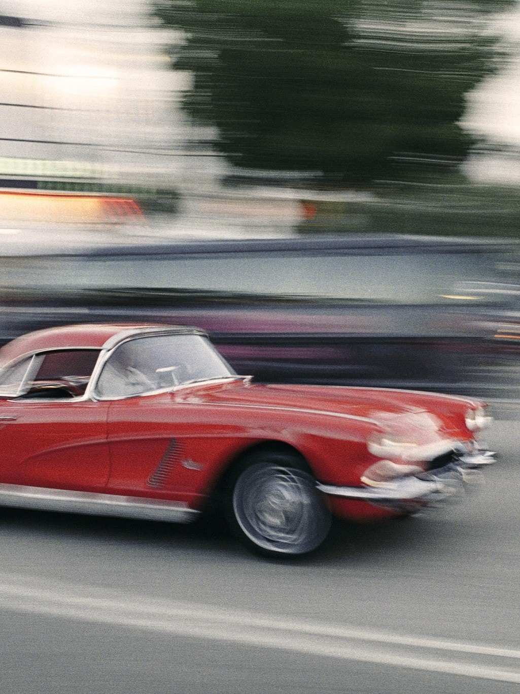 Ein rotes Vintage-Auto, wahrscheinlich ein klassischer Chevrolet Corvette, fährt mit hoher Geschwindigkeit auf einer Straße.