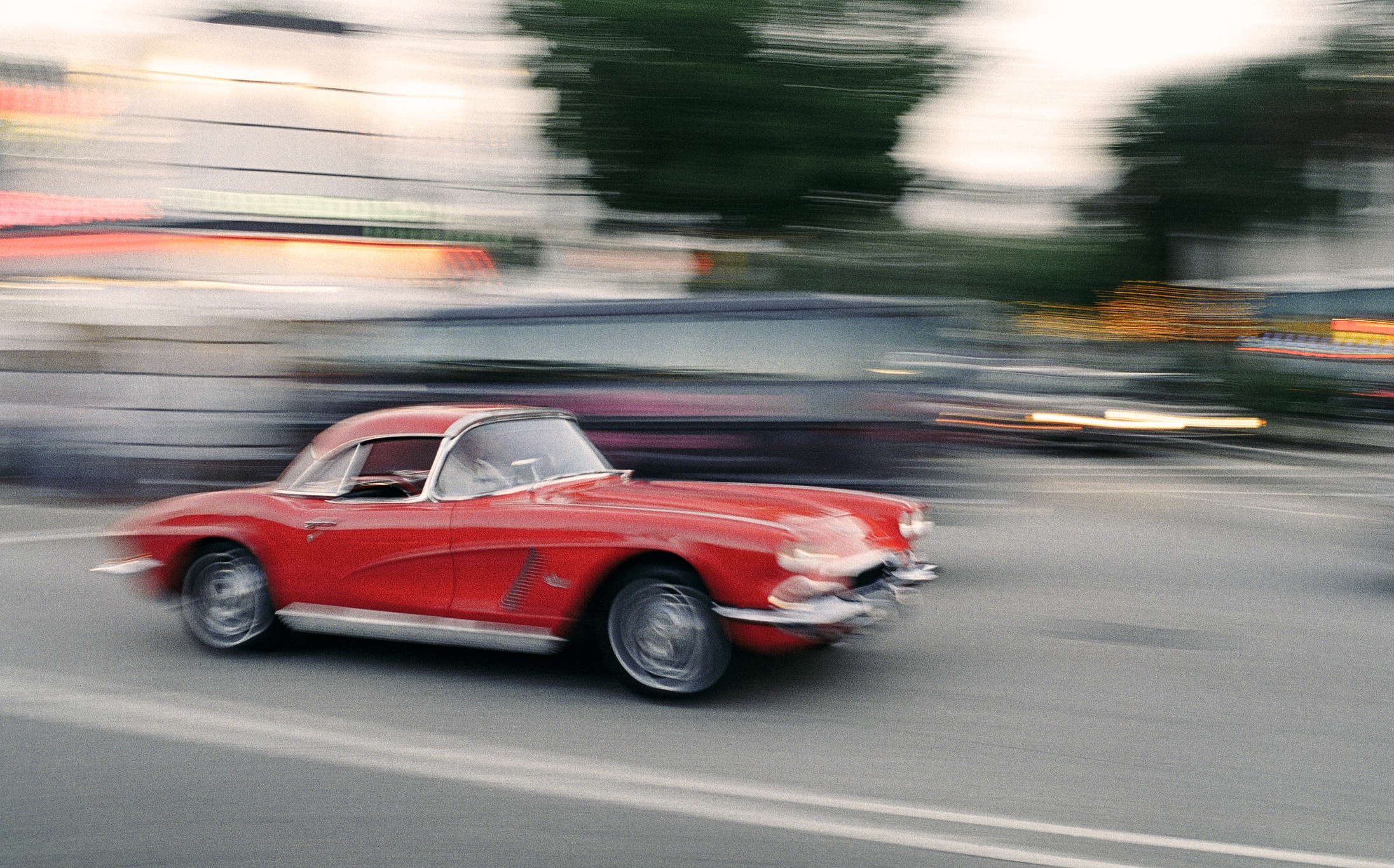 Ein rotes Vintage-Auto, wahrscheinlich ein klassischer Chevrolet Corvette, fährt mit hoher Geschwindigkeit auf einer Straße.