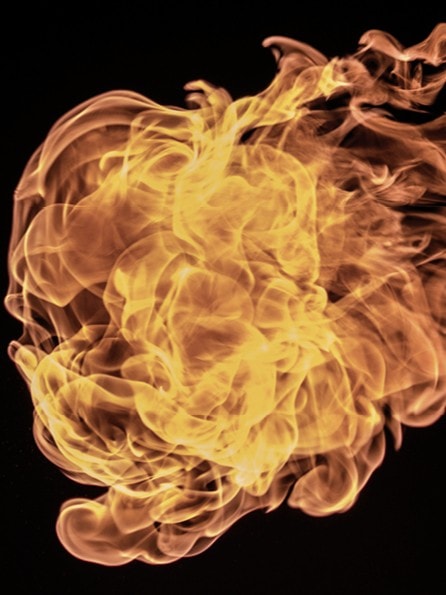 Ein dynamisches und komplexes Flammenmuster vor einem schwarzen Hintergrund. Die Flammen wirbeln und kräuseln sich, wobei sie verschiedene Gelb-, Orange- und Rottöne zeigen.