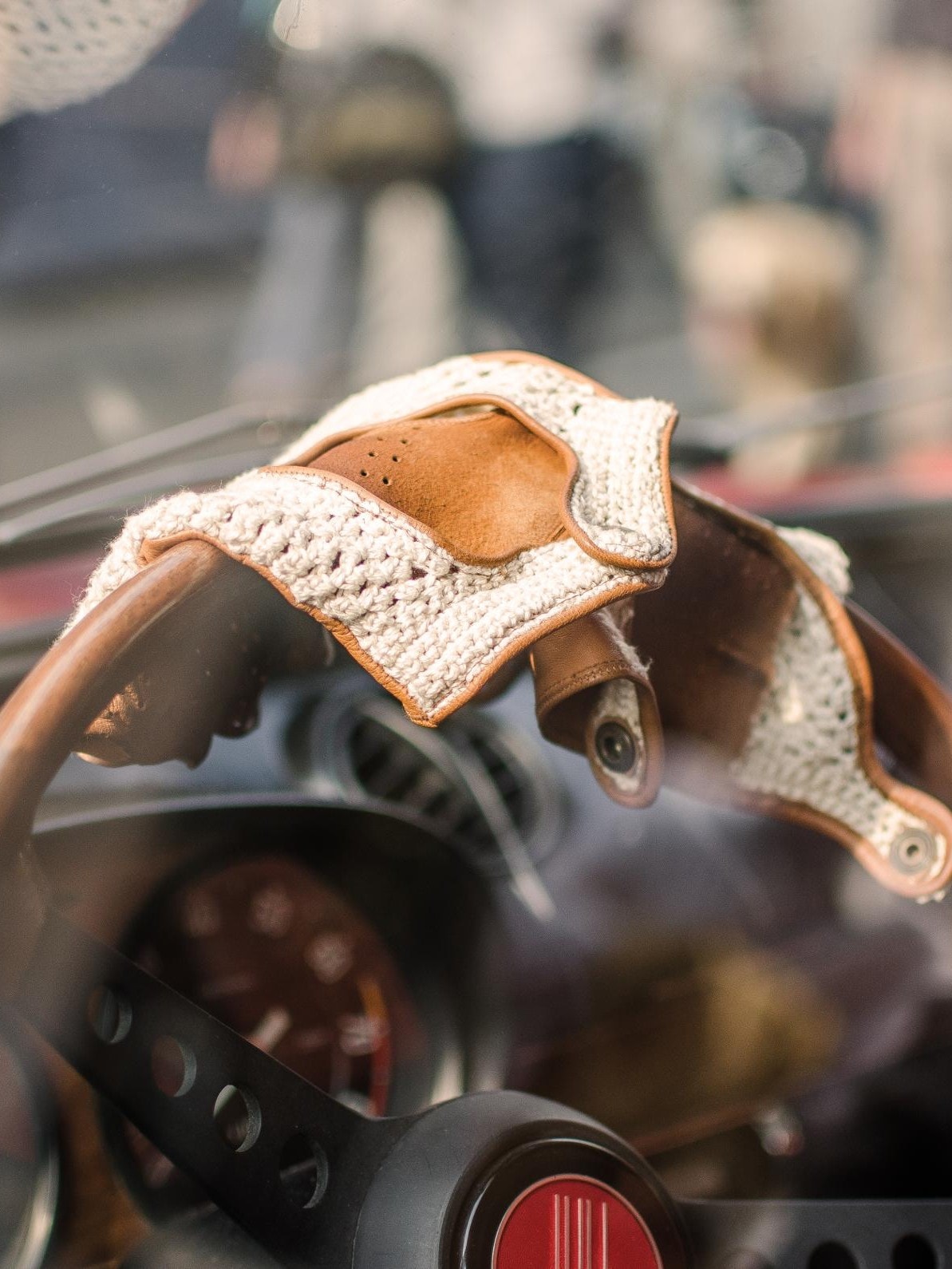 Ein Nahaufnahme des Lenkrads eines klassischen Autos mit darauf drapierten Vintage-Fahrerhandschuhen aus Leder und gehäkeltem Stoff.