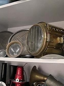 Ein Regal mit verschiedenen alten Schiffsleuchten und Laternen aus Messing. Die Leuchten haben unterschiedliche Größen und Formen und sind auf zwei Regalböden verteilt.