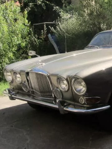 oldtimer import aus eu jaaEin klassischer Jaguar Mark X mit langer Motorhaube, Chromakzenten und runden Scheinwerfern, geparkt auf einer Auffahrt mit Grünfläche im Hintergrund.guar grossbritannien hiscox hochformat