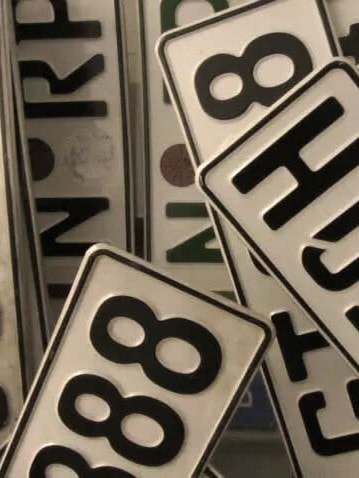 Ein Stapel von Fahrzeugkennzeichen, die sich überlappen. Ein auffälliges Kennzeichen in der Mitte trägt die Aufschrift "P25OSH", ein weiteres sichtbares Kennzeichen lautet "888".