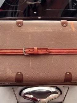 Ein brauner Vintage-Koffer mit Lederriemen ist auf der Rückseite eines klassischen Autos befestigt.