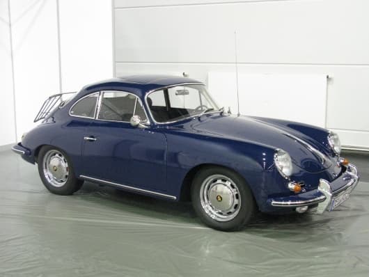 Ein dunkelblauer Oldtimer-Sportwagen Porsche 356 SC mit schlankem Design steht in einer Garage. Er hat eine runde Karosserie, Chromdetails und einen Gepäckträger am Heck.