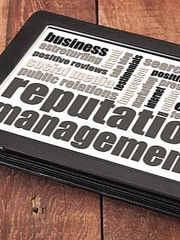 Tablet mit einer Wortwolke zum Thema "Reputation Management", auf einem rustikalen Holztisch liegend. Die Wörter umfassen Begriffe wie "business", "positive reviews", "public relations" und "ethics".