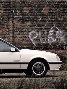 Weißer Opel Monza GSE parkt vor einer Backsteinwand mit Graffiti von Jens Tanz.