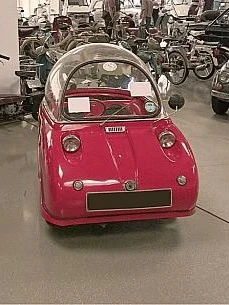 Blauer Peel P50, das kleinste Auto der Welt, parken in einem Oldtimer-Museum neben einem roten Variante Peel Trident