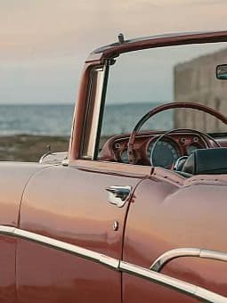 Ein rotes Cabrio, das in der Nähe einer Küste mit dem Ozean im Hintergrund geparkt ist.