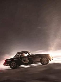 Ein schwarzes Vintage-Sportauto mit der Nummer 12, das mit hoher Geschwindigkeit durch eine verschneite oder vereiste Umgebung fährt.