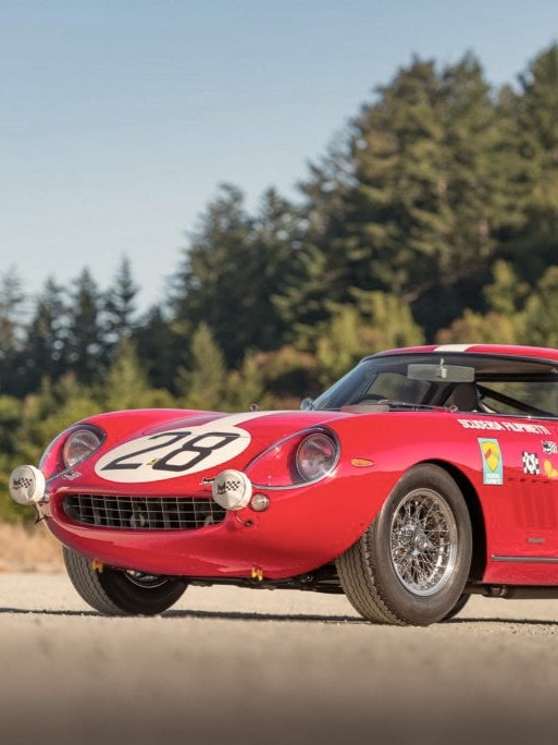 Roter Vintage-Rennwagen mit der Nummer 28 auf Motorhaube und Seiten, geparkt auf einem Feldweg vor Bäumen und klarem Himmel.