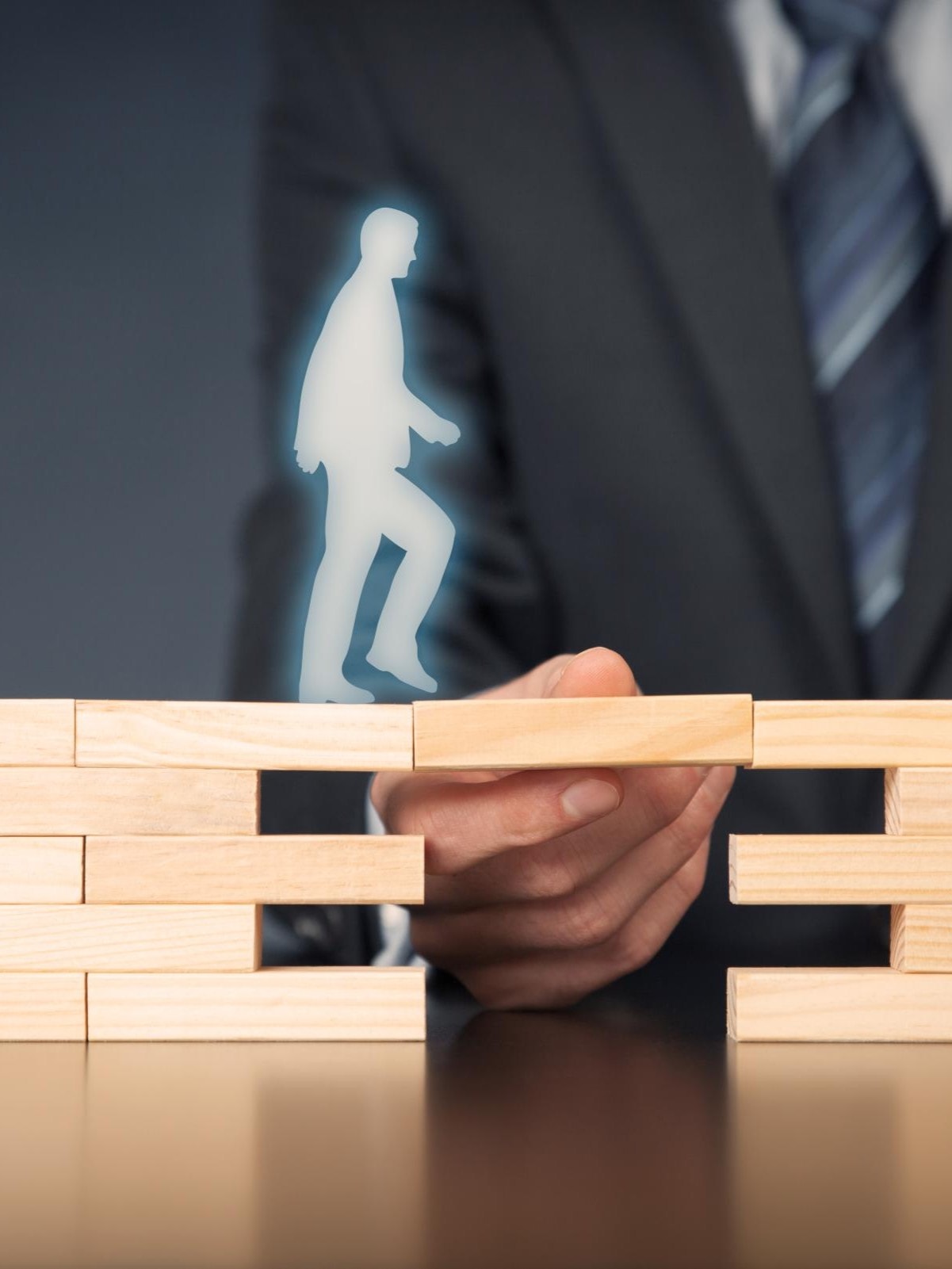 Person im Anzug legt einen Holzblock zwischen zwei Stapel, auf dem eine leuchtende Silhouette eine Treppe hinaufgeht – Symbol für Fortschritt.