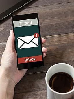 E-Mail-Benachrichtigung auf Smartphone: Person hält Smartphone und Kaffeetasse in der Hand