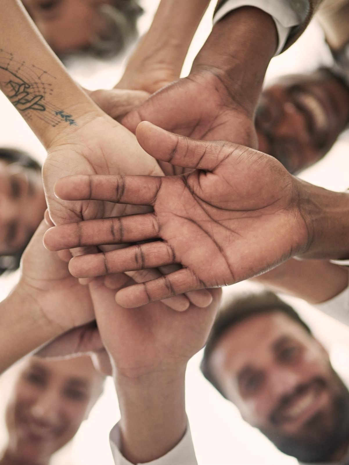 Teamwork und Zusammenarbeit: Gruppe von Menschen legt die Hände übereinander in Zeichen der Einheit
