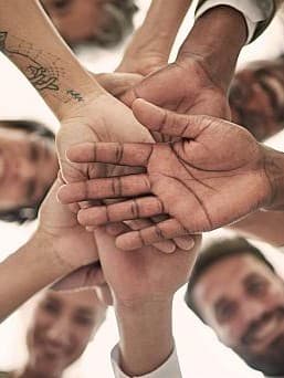 Teamwork und Zusammenarbeit: Gruppe von Menschen legt die Hände übereinander in Zeichen der Einheit