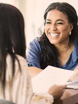 Freundliches Gespräch zwischen zwei Geschäftsfrauen: Austausch von Dokumenten in professioneller Umgebung