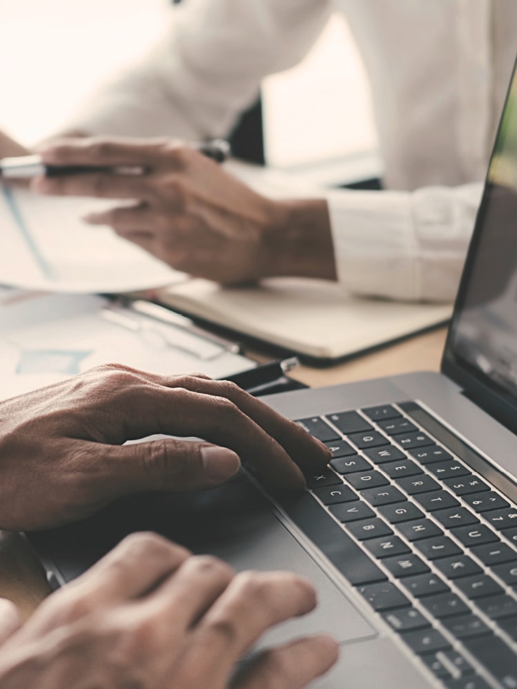 Zwei unbekannte Männer arbeiten an einem Laptop und an Dokumenten