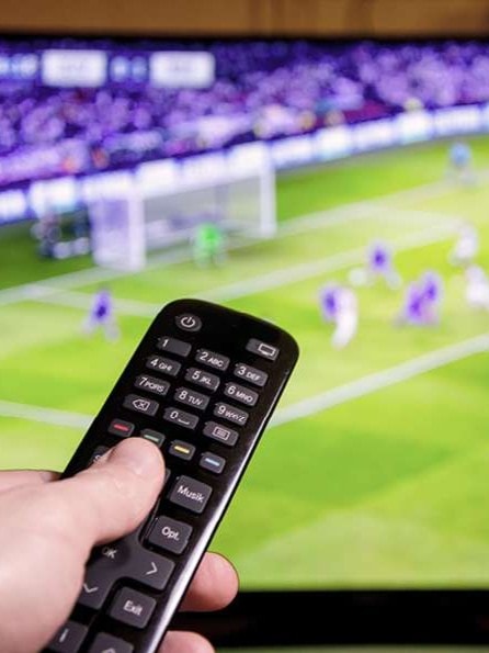 Fußballspiel läuft in Fernseher und wird live übertragen. Hand hält eine Fernbedienung vor den TV.
