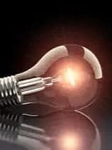 Nahaufnahme einer liegenden Glühbirne mit eingeschaltetem Glühfaden auf schwarzem, reflektierendem Untergrund