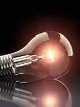 Nahaufnahme einer liegenden Glühbirne mit eingeschaltetem Glühfaden auf schwarzem, reflektierendem Untergrund