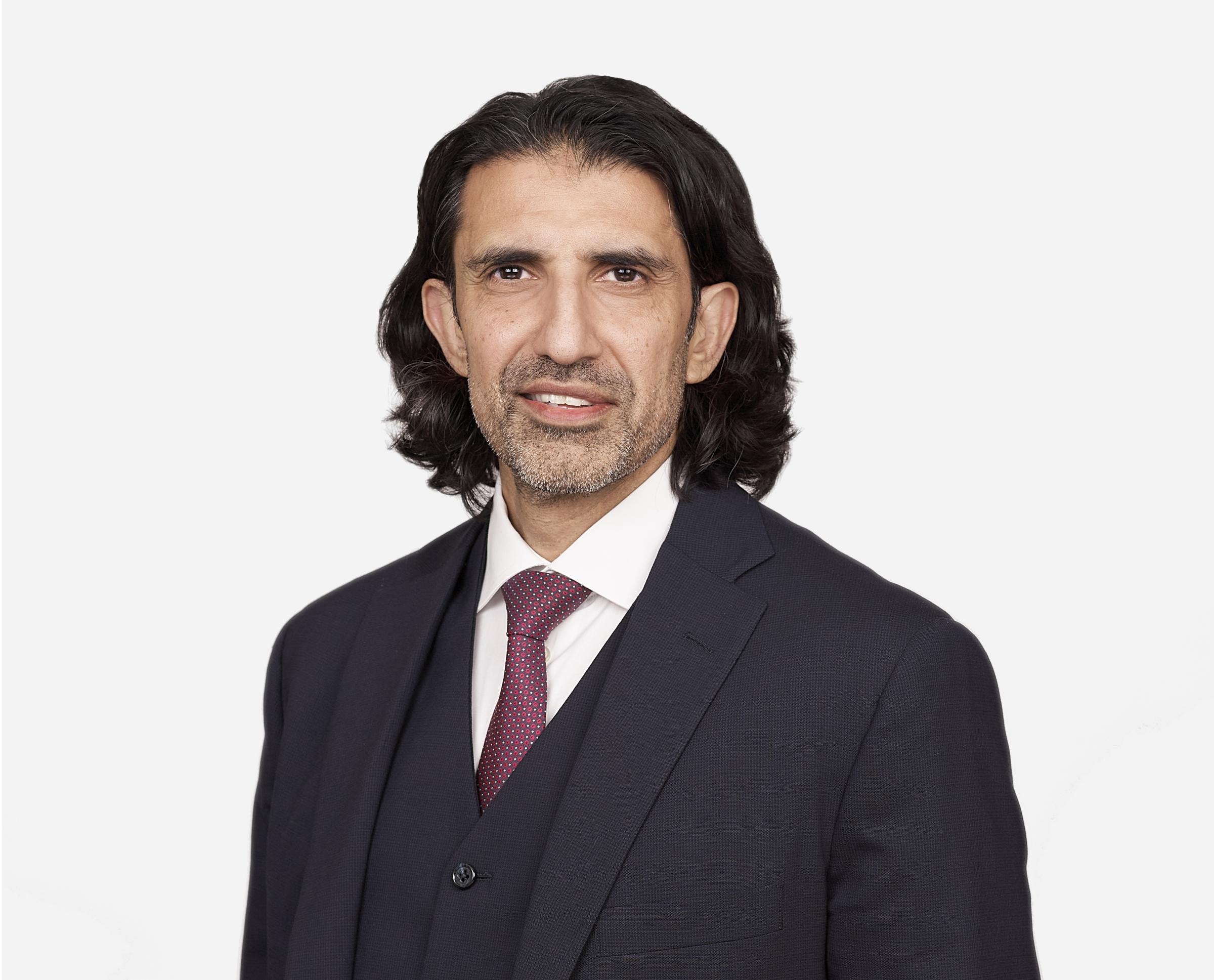 Bild von Aki Hussain, dem CEO der Hiscox Group, in einem schwarzen Anzug mit Krawatte.