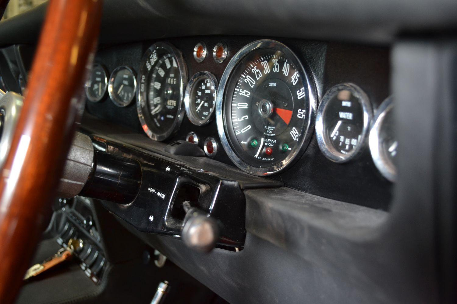 Detailansicht des Armaturenbretts eines klassischen Autos mit verschiedenen Instrumentenanzeigen und einem hölzernen Lenkrad