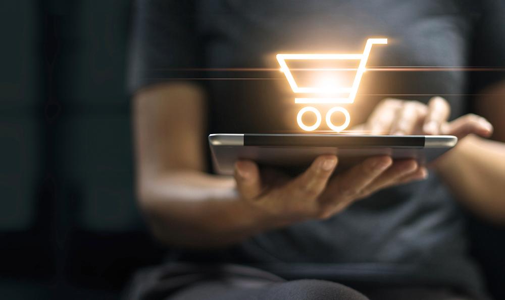 E-Commerce: Person nutzt Tablet mit leuchtendem Einkaufswagen-Symbol für Online-Shopping
