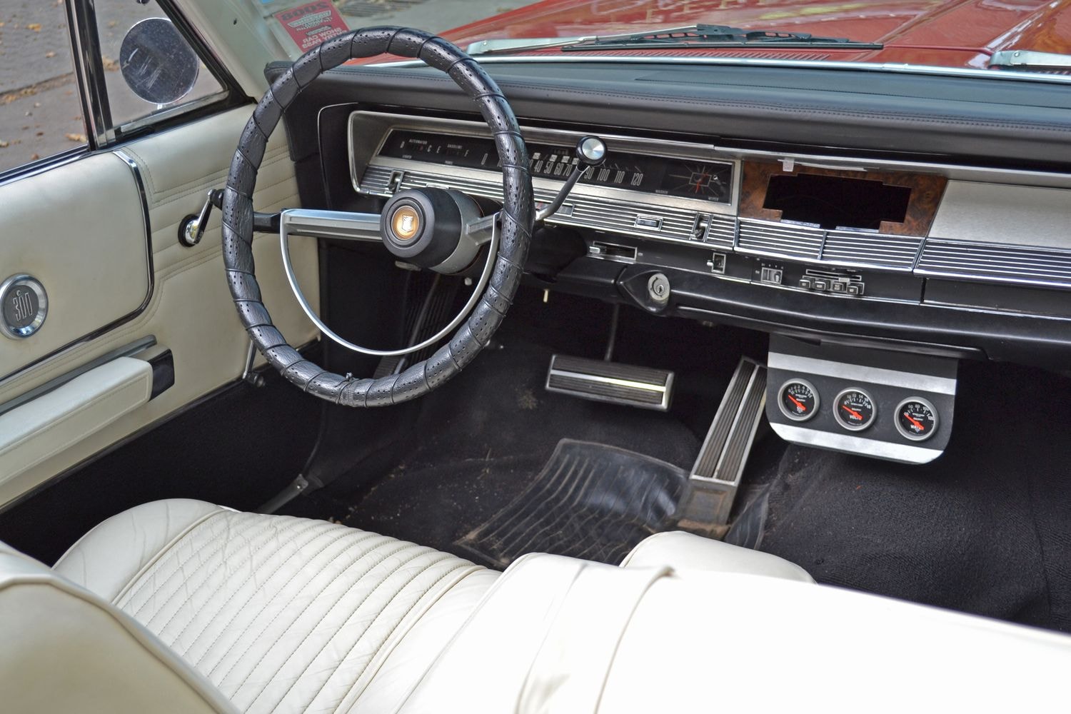 Das Innere eines klassischen Autos mit einem schwarzen Lenkrad, weißer Lederausstattung und einem Armaturenbrett mit verschiedenen Instrumenten.