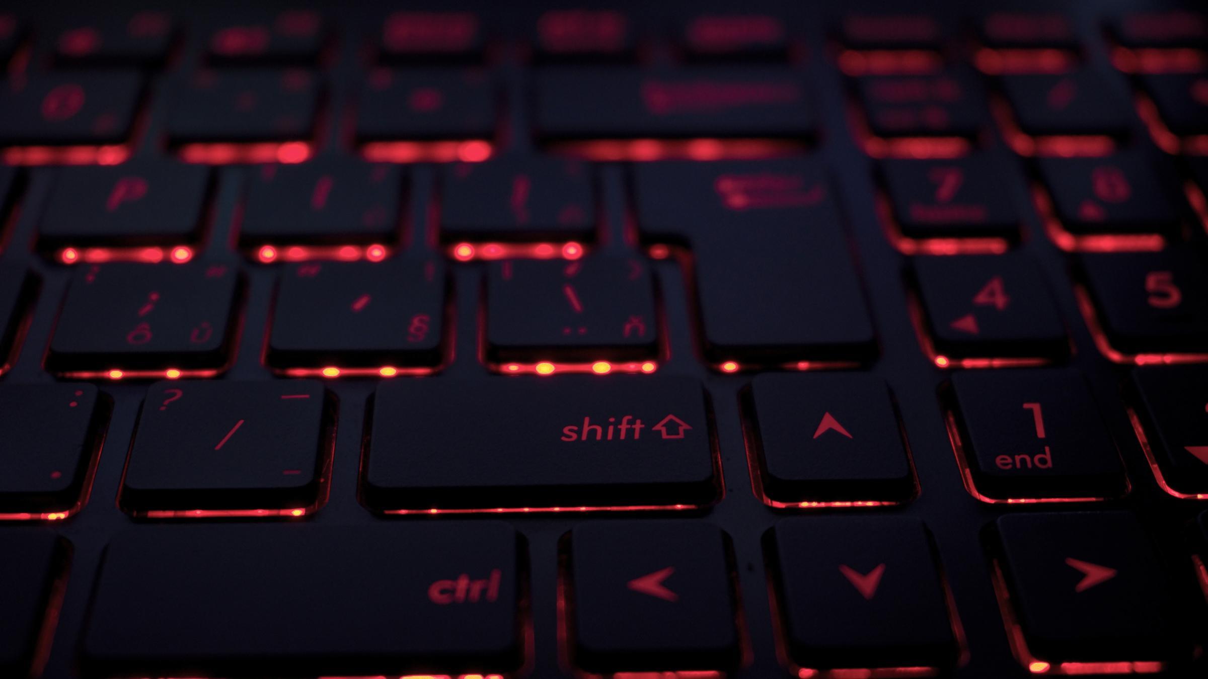Eine Nahaufnahme einer Tastatur mit roter Hintergrundbeleuchtung. Die Tasten sind schwarz und die rote Beleuchtung scheint durch die Buchstaben und Symbole auf den Tasten hindurch.