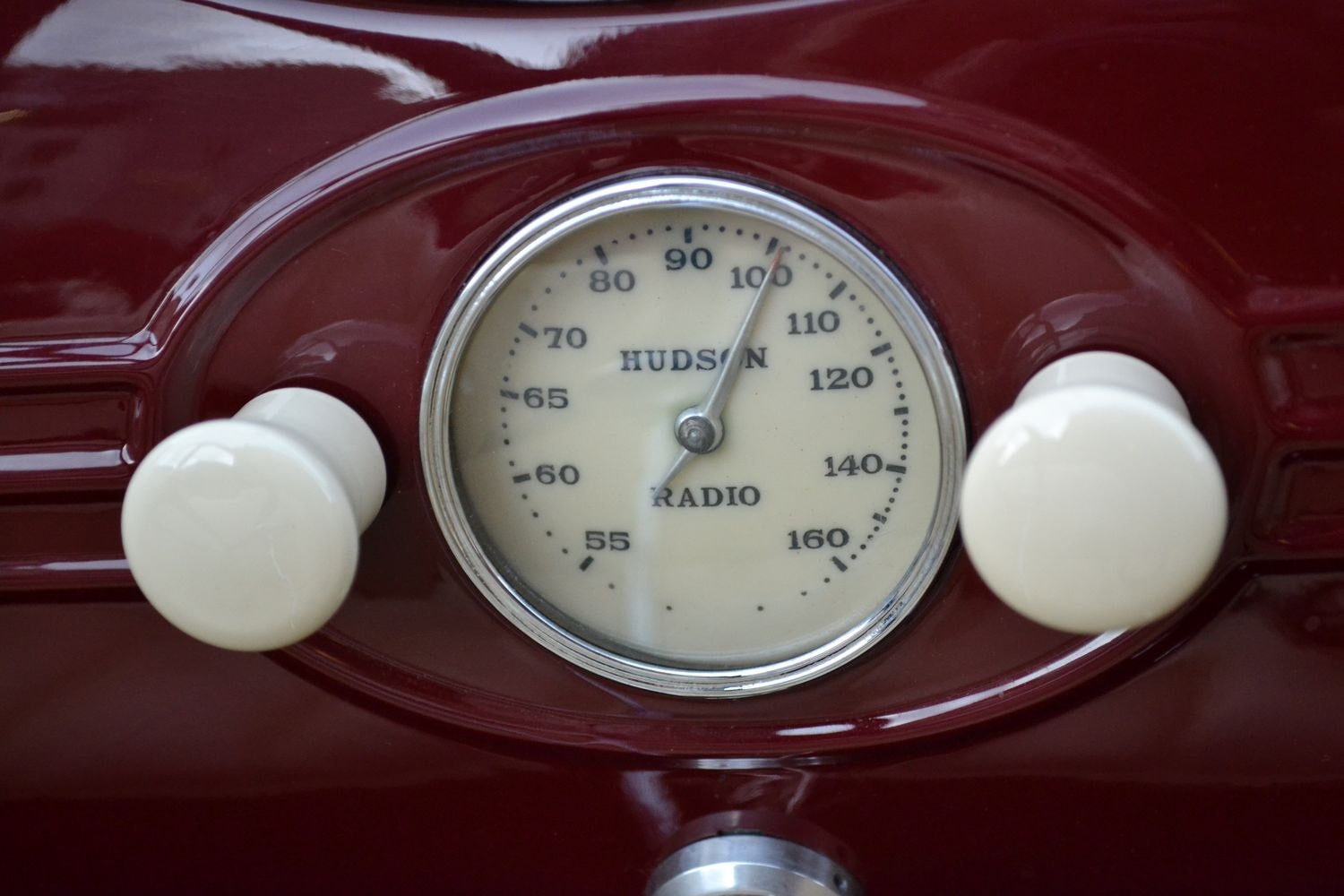 Ein altes Autoradio mit einer runden Skala, die von 55 bis 160 reicht. In der Mitte der Skala steht 'HUDSON RADIO'. Links und rechts der Skala befinden sich zwei weiße Drehknöpfe.