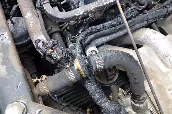 Ein Nahaufnahme des Motorraums mit mehreren Schläuchen und Kabeln. Die Schläuche weisen sichtbare Schäden auf, mit Anzeichen von Verbrennungen oder Schmelzen.